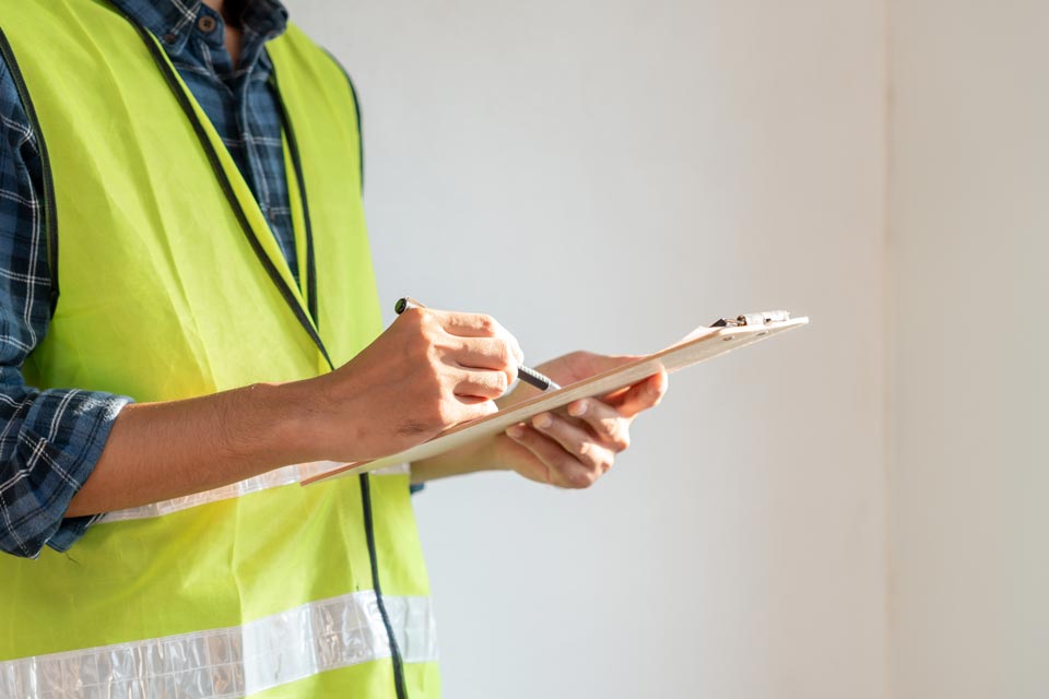 close-up-man-with-noen-construction-safety-vest-holding-clipboard-pen